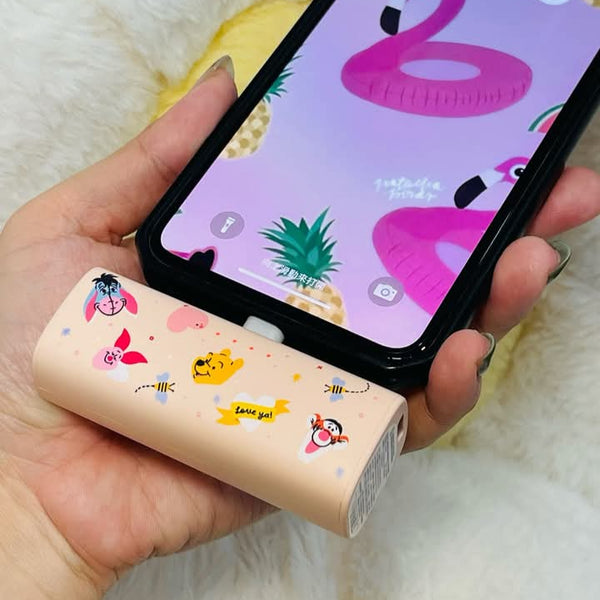 Hand holding a phone with a colorful screen and a small cylindrical product with cartoon designs.