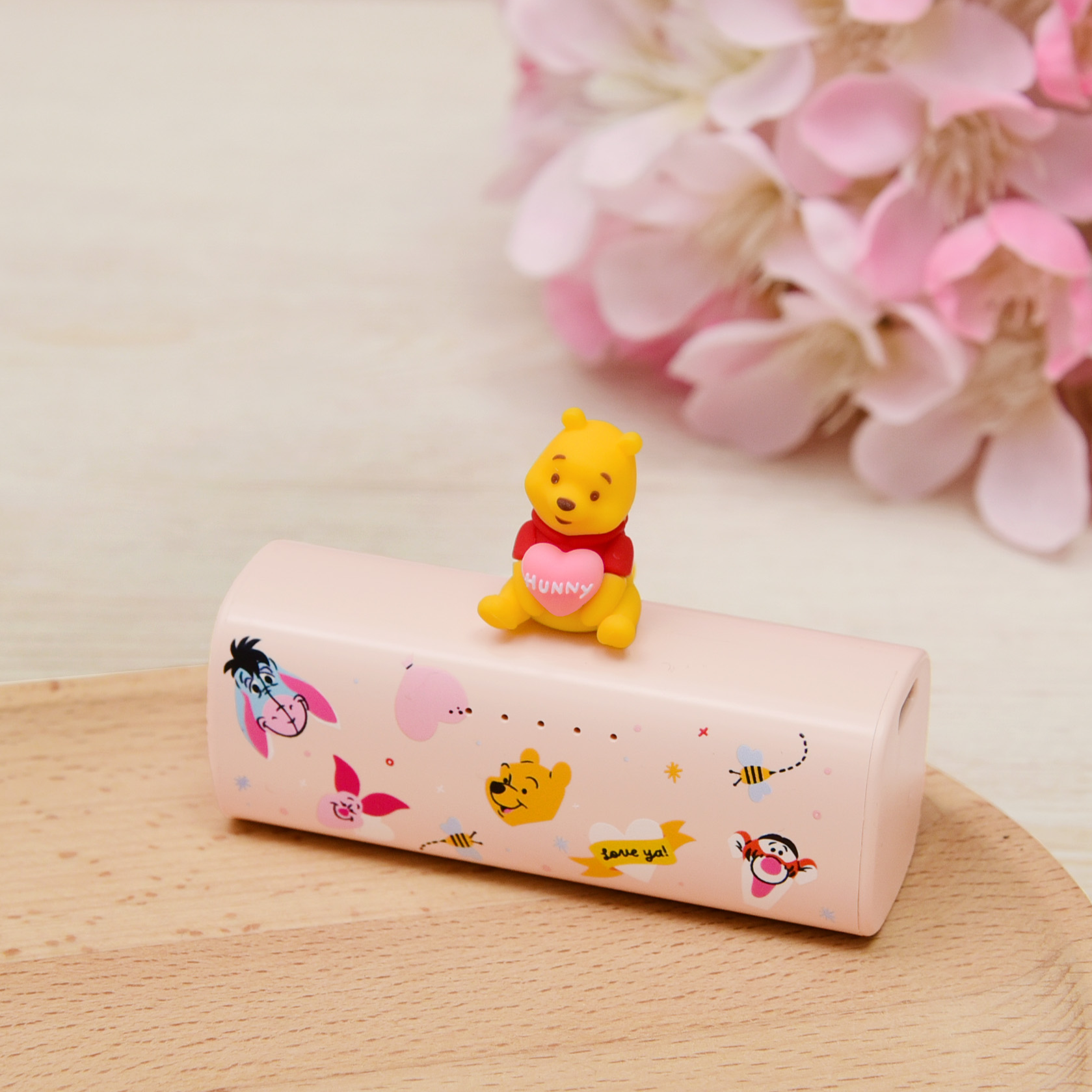 Power bank with cartoon characters and a small figurine on top, set against a light background with pink flowers.