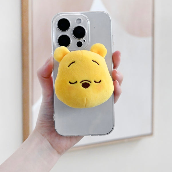 Phone case with a yellow plush bear attachment held by a hand against a neutral background